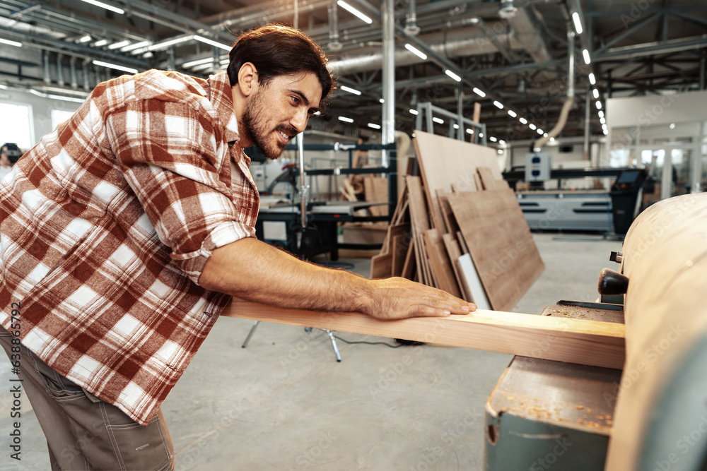 Young carpenter working on woodworking machines in the furniture factory