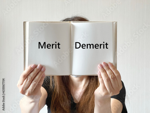 顔の前でMeritとDemeritの文字入り本のページを開く女性