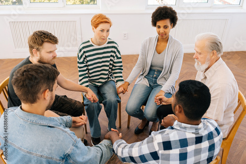 Top view portrait of diverse group of addicted people sitting in circle and holding hands crosswise during therapy meeting. Concept of group consulting of mental health problem.
