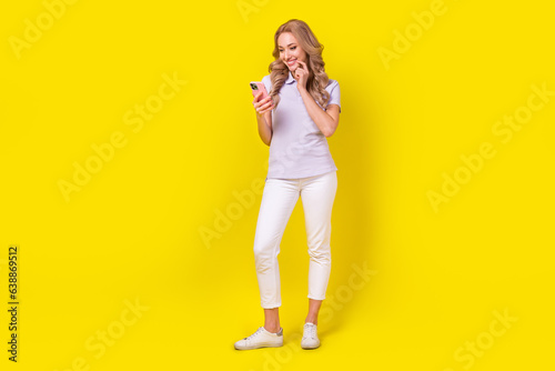 Full size photo of lovely nice cute girl wear violet polo white trousers read email in smartphone isolated on yellow color background