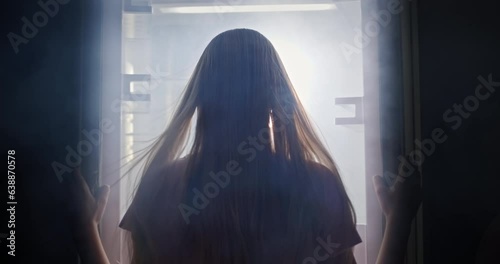 A young woman opens the refrigerator doors side by side. From there the wind blows and the fog goes. photo