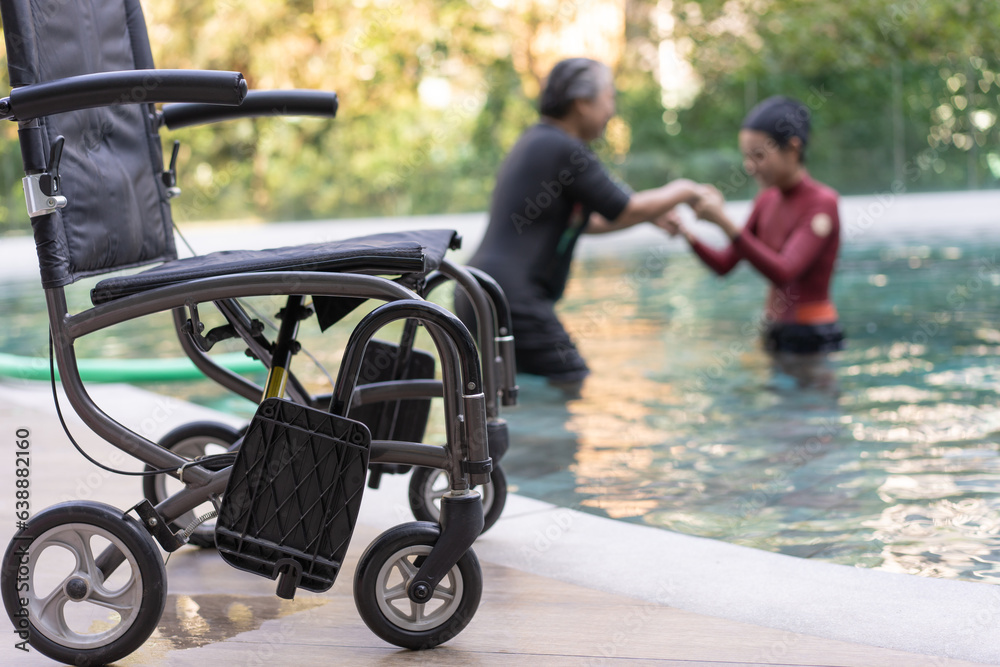 Naklejka premium Selective focus off wheelchair background of physical therapist helping senior woman in aqua, old women and mature doing aqua aerobics exercise in swimming pool, Elderly sports, and active lifestyle.