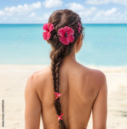 Jolie fille blonde de dos portant une jolie natte et des fleurs d'hibiscus sur la plage en été. 