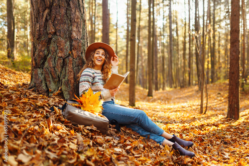 Beautiful woman with curly hair with a book on a bicycle sits on fallen leaves in the autumn forest. Concept of autumn walks, relax.