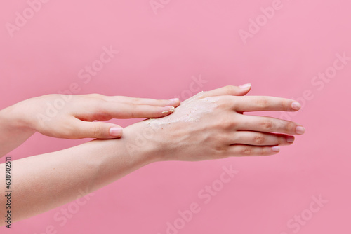 Horizontal image of beautiful  tender young woman hands usinging cream  scrub on her hands on pastel pink background. Anti-aging.