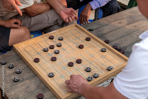 High angle view of the board of Xiangqi game, also called Chinese chess or elephant chess with hands of players and observers around board on the Sunday Market in Bac Ha, Vietnam photo