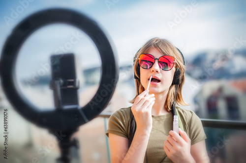 Influencer young woman recording video on smartphone and lighting herself with ring lamp. Broadcast communicates with followers in social networks.