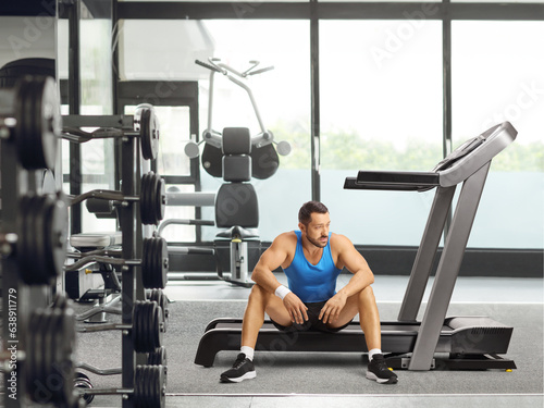 Athlete man sitting on a treadmill and thinking at a gym