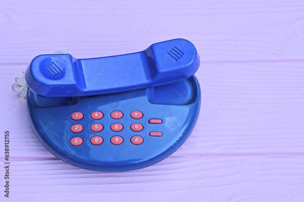 one small old blue plastic phone toy with red buttons lies on a pink wooden table one small old blue plastic phone toy with red buttons lies on a pink wooden table