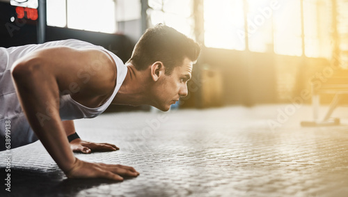 Fitness, push up and man for training, strong exercise and focus in gym with muscle health on floor. Athlete, bodybuilder or young sports person with shoulder or arm workout and motivation on ground