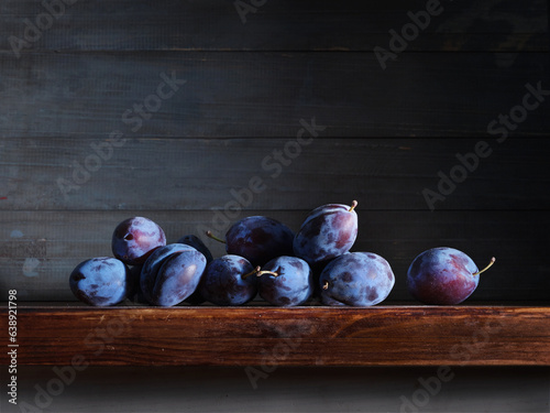Image of Still Life with stack of Plums. Dark wood background, antique wooden table.