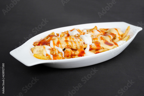 Loaded fries potatoes with creamy cheesy sauce isolated on black background              