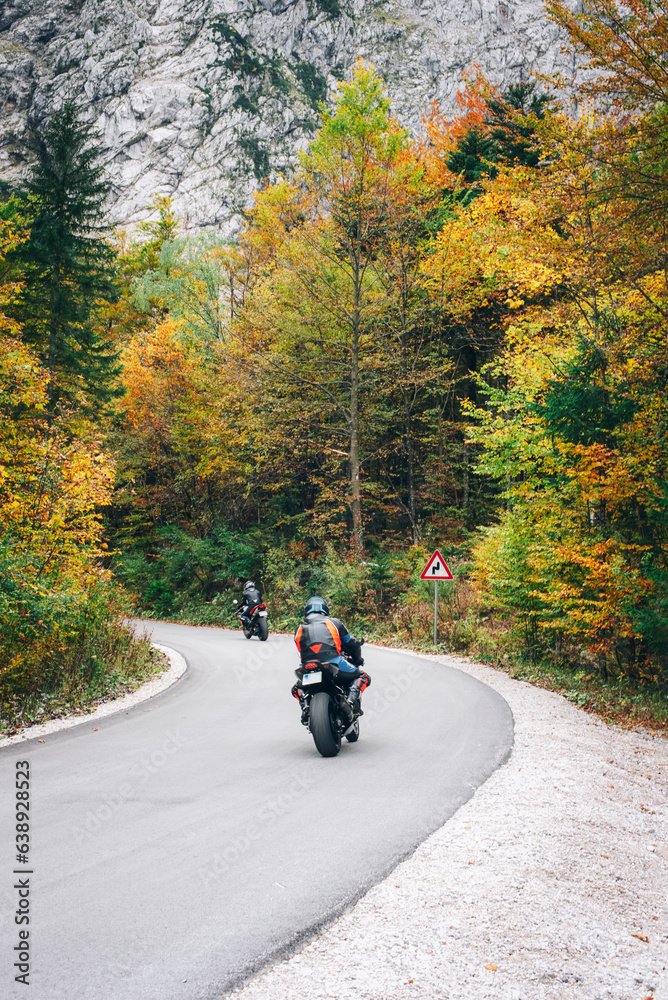 Motorcyclists ride on the road through the autumn forest in the mountains Motorcyclists ride on the road through the autumn forest in the mountains
