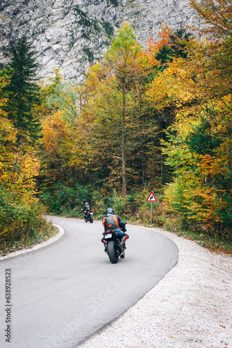 Motorcyclists ride on the road through the autumn forest in the mountains