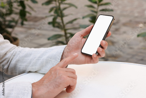 Man using smartphone at white table outdoors, closeup