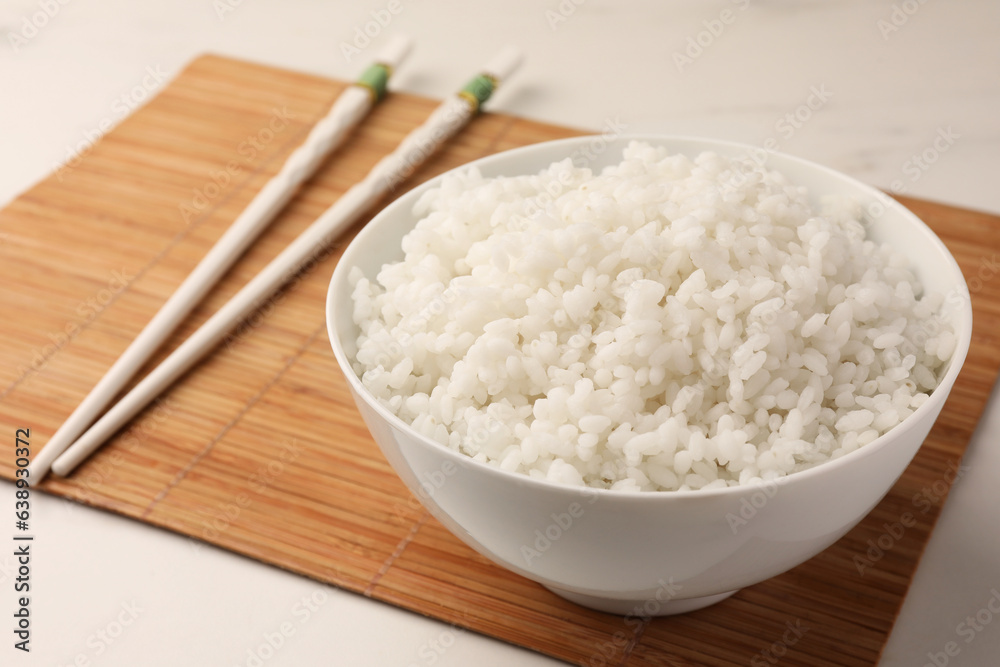Bowl with delicious rice and chopsticks on white table Bowl with delicious rice and chopsticks on white table