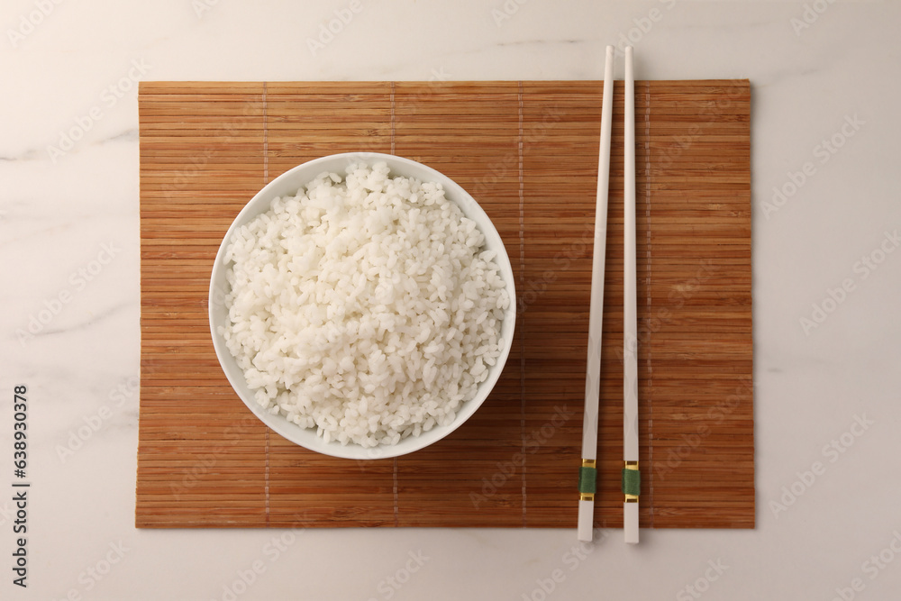 Bowl with delicious rice and chopsticks on white marble table, top view Bowl with delicious rice and chopsticks on white marble table, top view