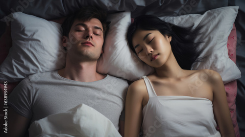 Snoring man. Couple in bed, men snoring and women can not sleep, covering ears with pillow for snore noise. Young interracial couple, Asian woman, Caucasian men sleeping in bed at home. photo
