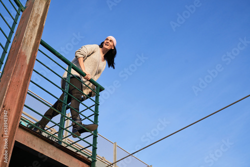 Cheerful ethnic woman in pink scarf leaning on metal fence © ADDICTIVE STOCK CORE