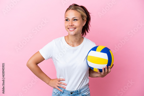 Young Russian woman playing volleyball isolated on pink background posing with arms at hip and smiling