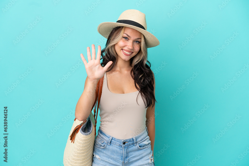 Fototapeta premium Teenager Russian girl with pamel and beach bag isolated on blue background counting five with fingers