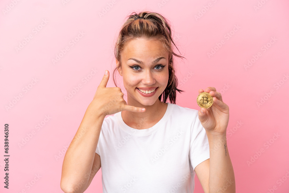 Teenager Russian girl holding a Bitcoin isolated on pink background making phone gesture. Call me back sign Teenager Russian girl holding a Bitcoin isolated on pink background making phone gesture. Call me back sign