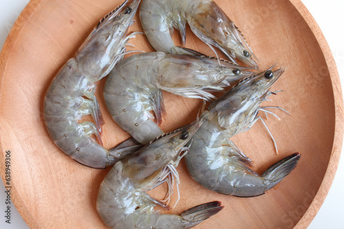 Uncooked whiteleg shrimps or Litopenaeus vannamei, on a wooden plate. Isolated on white background photo