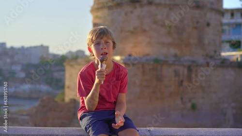 A little boy is eating a Turkish ice cream sitting in front of the Hidirlik tower in the historical part of the city of Antalya, Turkey. photo