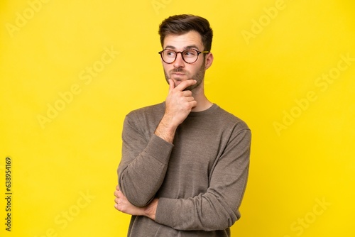 Foto Young caucasian man isolated on yellow background having doubts and thinking