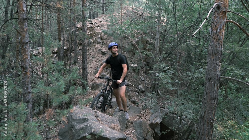 mountain bike.A man in a protective helmet walks with a mountain bike on a rocky terrain.Active lifestyle