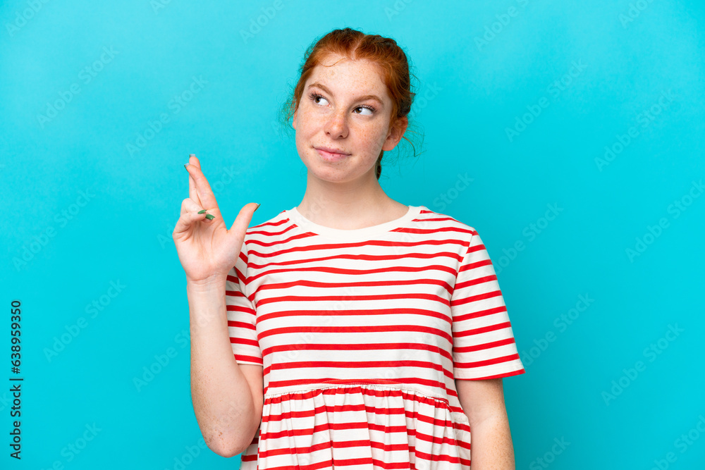 Young reddish woman isolated on blue background with fingers crossing and wishing the best Young reddish woman isolated on blue background with fingers crossing and wishing the best