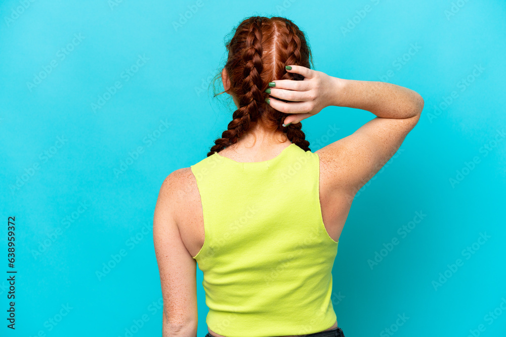 Young reddish woman isolated on blue background in back position and thinking