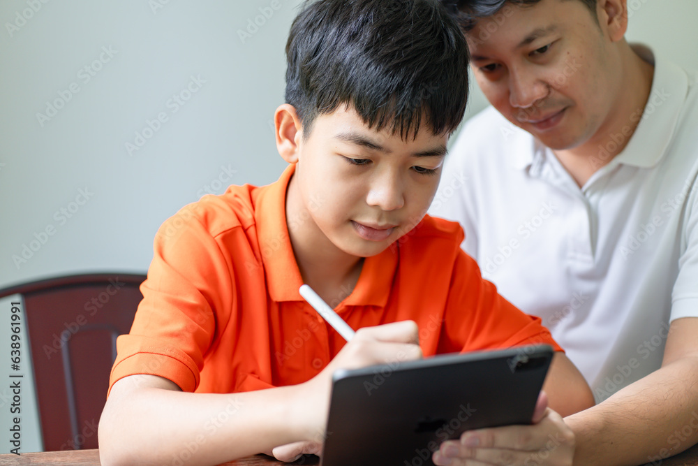 Asian father and son using tablet teaching son to draw.playing with digital tablet at desk fatherhood