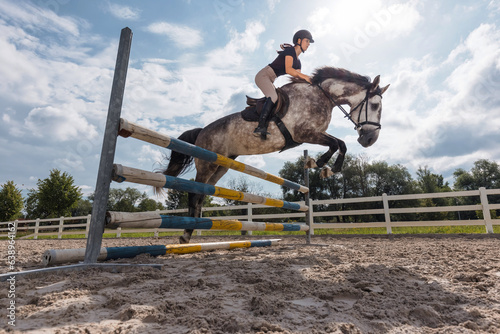 Vászonkép Showjumping gray horse with female jockey, jumping over hurdles, on a sunny day