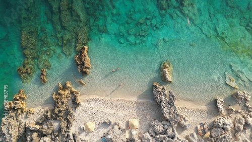 Aerial view of a rocky coastline with light sand. Crystal clear and calm sea waters.