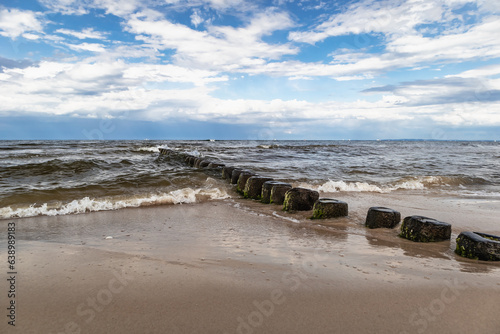 Brzeg Morza Bałtyckiego z falochronami i błękitnym niebem z chmurami. Baltic sea shore with breakwaters and blue sky with clouds.