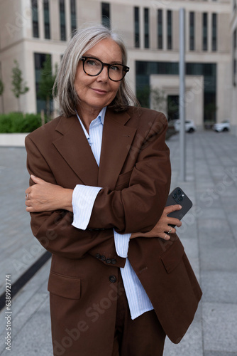 charming mature woman with gray hair in a stylish suit walks around the city
