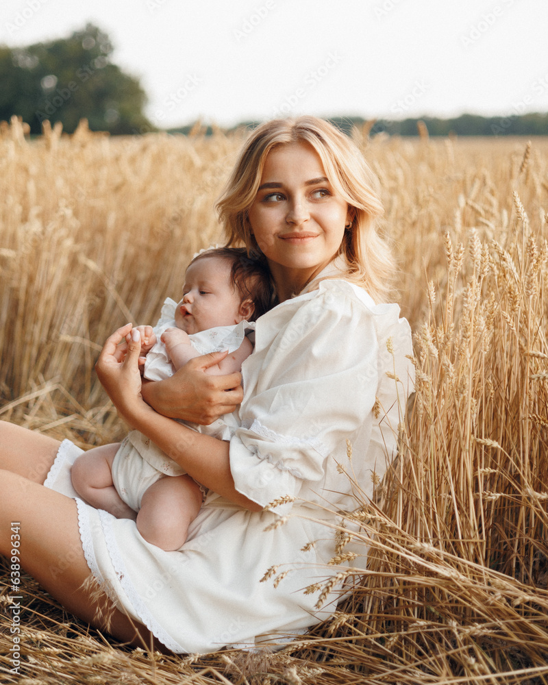 Portrait of a charming attractive young woman mother blonde in a straw hat and white dress in a field of ripe golden wheat holds her little daughter child in her arms at sunset Portrait of a charming attractive young woman mother blonde in a straw hat and white dress in a field of ripe golden wheat holds her little daughter child in her arms at sunset
