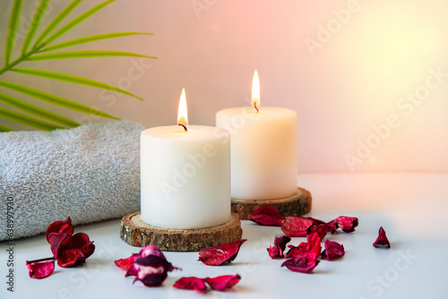 Relaxing spa concept with two white candles on a wooden podium and green palm leaf and towel