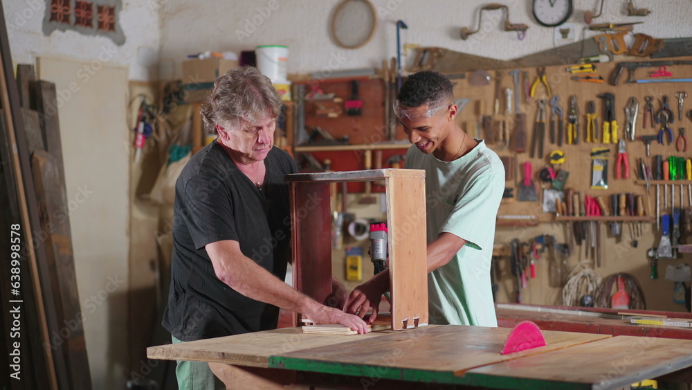 Senior carpenter guiding younger apprentice at carpentry workshop. Job occupation apprenticeship, mentor orienting and helping junior worker with craftmanship furniture
