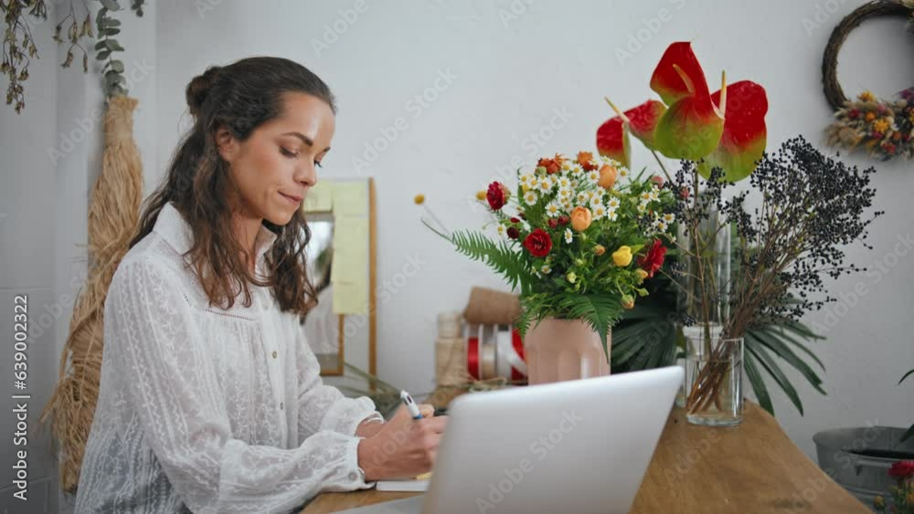 Focused entrepreneur work flowers shop table. Woman florist write notes in store Focused entrepreneur work flowers shop table. Woman florist write notes in store