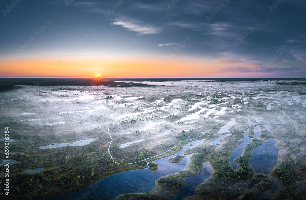 Obraz premium Colorful morning sunrise over the bog of national park of Ķemeri. Wooden trail leading through wetlands covered in fog. 