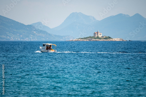 Small boat passing in front Velika Sestrica island with famous stone lighthouse in the background in the Peljesac canal, Croatia photo