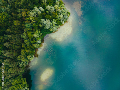 Aerial drone top down view of lake among forest with beautiful turquoise water in summer day.  © nikkimeel