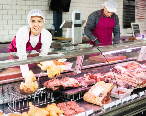 Happy female butcher holding whole chicken in meat section of supermarket