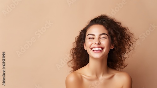 Portrait of smiling girl enjoying beauty treatment on beige background. Beautiful natural woman looking at copy space, spa and wellness concept. Carefree laughing woman with bare shoulders isolated.