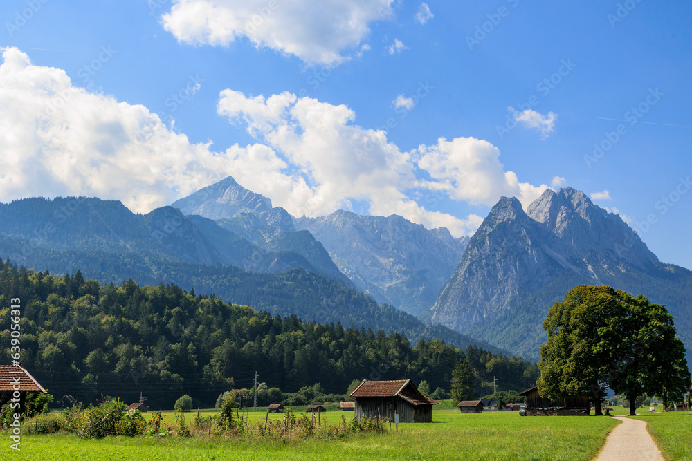 Field path near Garmisch-Partenkirchen with view to the Zugspitz massif on a sunny day with blue sky and white cumulus clouds Field path near Garmisch-Partenkirchen with view to the Zugspitz massif on a sunny day with blue sky and white cumulus clouds