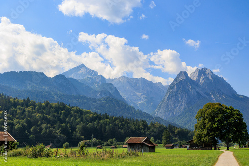 Field path near Garmisch-Partenkirchen with view to the Zugspitz massif on a sunny day with blue sky and white cumulus clouds