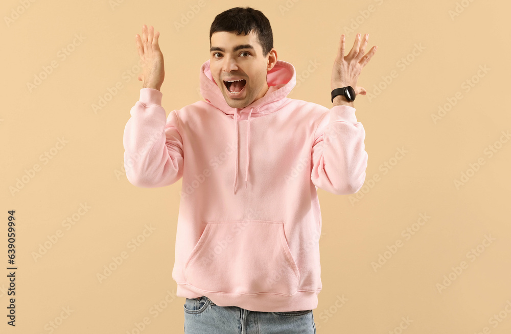 Stressed young man in hoodie and with watch on beige background