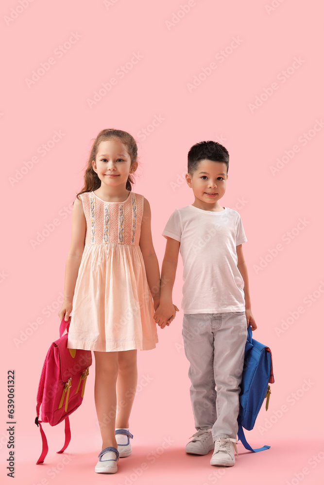 Cute little pupils with backpacks holding hands on pink background Cute little pupils with backpacks holding hands on pink background